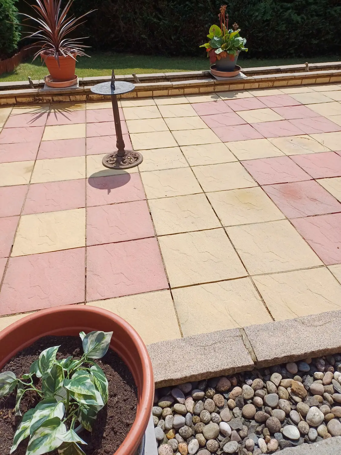 Red and cream checkerboard patio paving with a brass sundial and a planted pot after professional cleaning