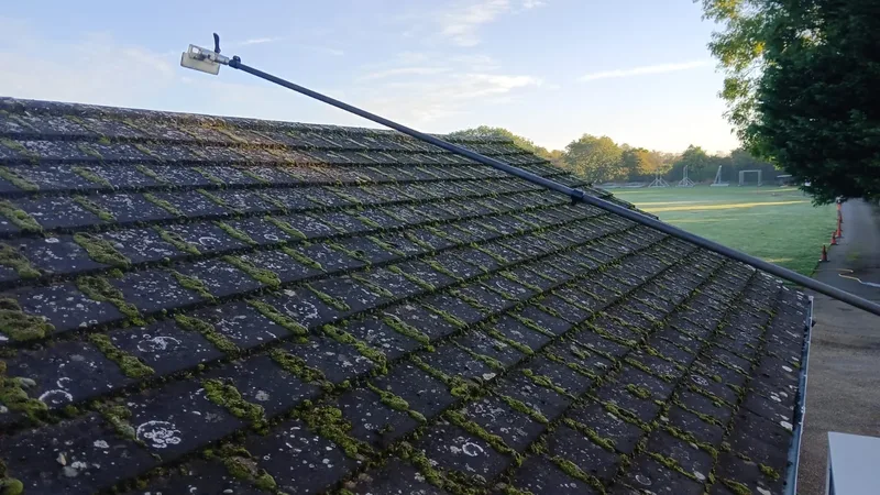 Professional pressure washing equipment being used to clean moss from a residential roof - Exterior Cleaning Solutions