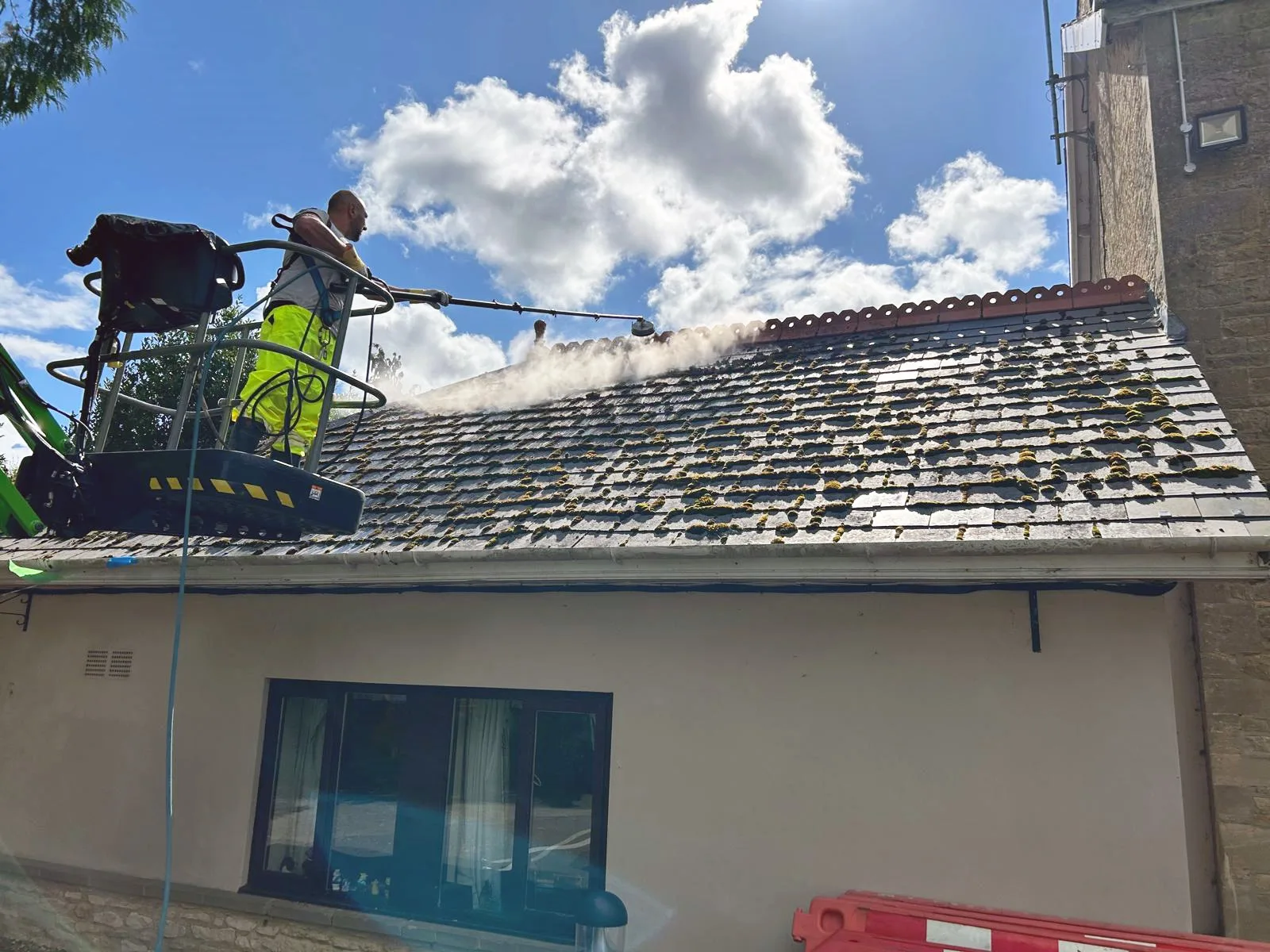 Exterior Cleaning Solutions technician cleaning a mossy roof from a cherry picker platform - professional access for safe roof maintenance