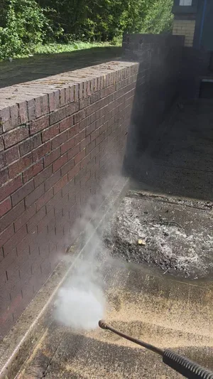 During - commercial red brick wall base pressure washed algae debris removal, Rugby.