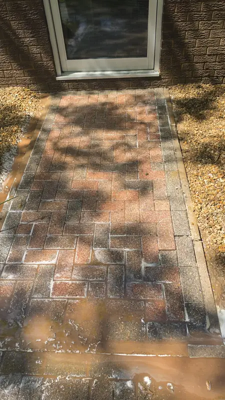 Brick paving path with the lower half cleaned to a vibrant red while the upper half remains darker and weathered