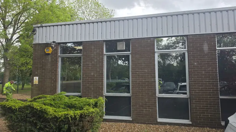 Wide shot of the side facade with three tall windows, ADT alarm sign, brick and cladding showing visible weathering