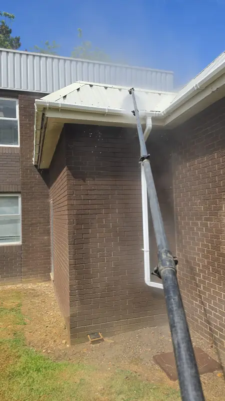 Low-pressure rinse applied to the corner of the entrance canopy cladding with water droplets visible spraying away in the air