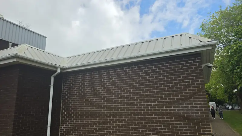 Wide view of the side wall - brown brickwork below, continuous cladding band above, two pedestrians on the pavement