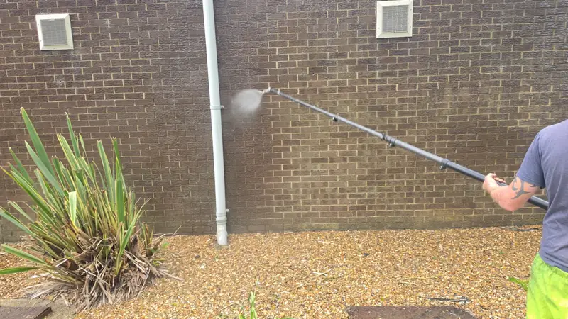 Soft wash applied at the base of the brick wall beside iris and yucca planting, a second operator partly visible to the right