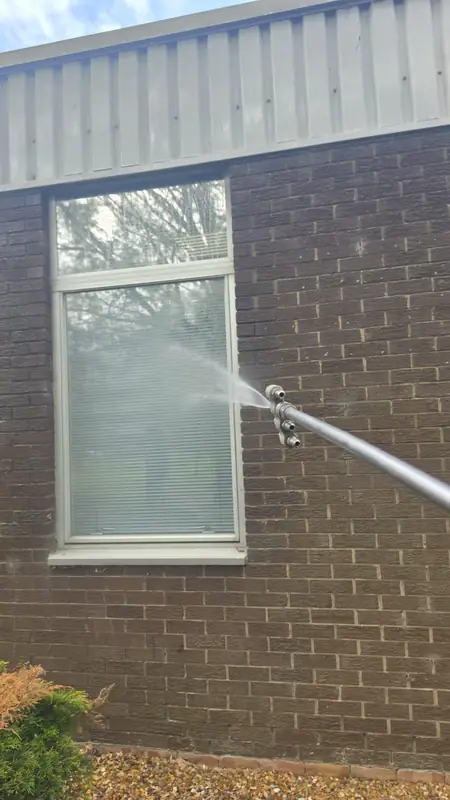 Soft wash directed at the lower frame of a tall window where dirt accumulates against the brickwork
