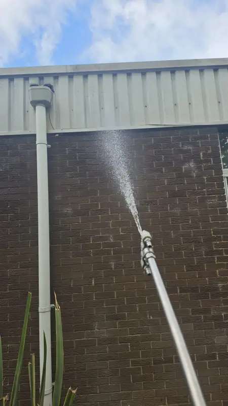 Low-pressure soft wash solution applied to brick wall directly under the cladding band with downpipe visible