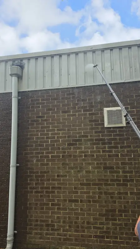 Soft wash fan spray reaching the top edge of grey corrugated metal cladding above the brick wall