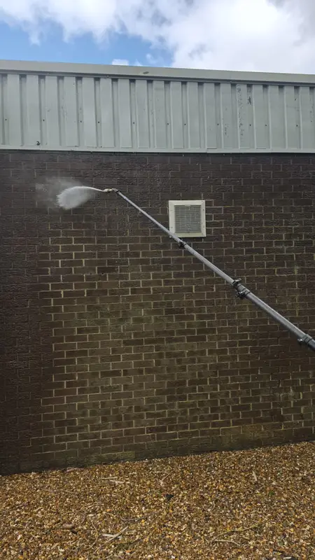 Wider view of brick wall with white ventilation grille and downpipe being soft washed in a single pass