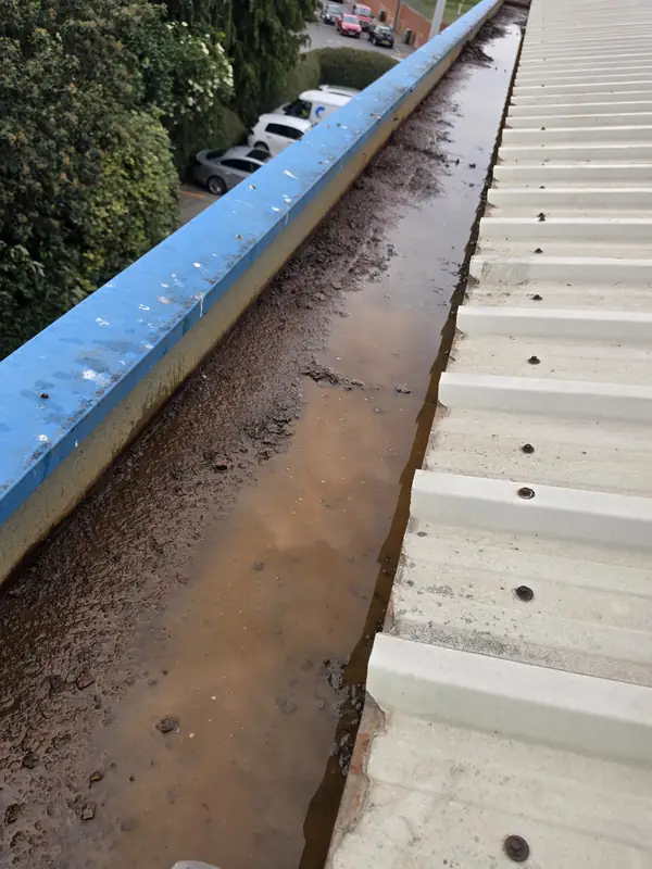 Longitudinal view of an emptied gutter showing extensive brown-orange rust along the full surface and stagnant water at the base