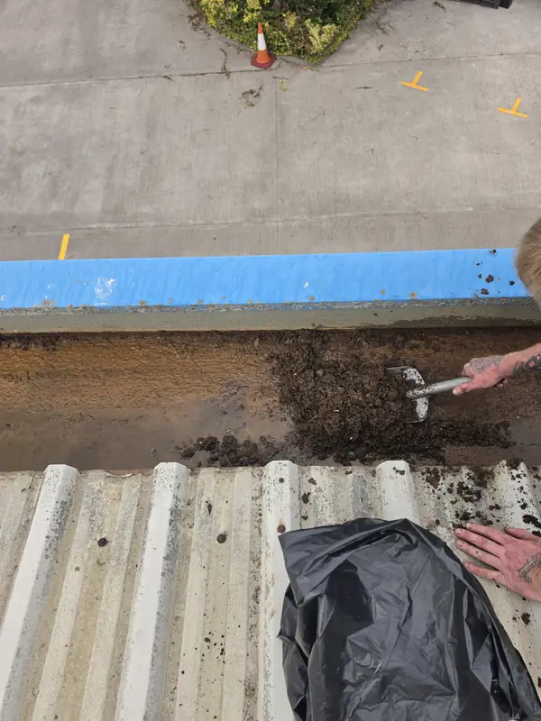 Close-up showing a clear division between a freshly cleared rust-yellow section of gutter and an adjacent section still full of dark mud