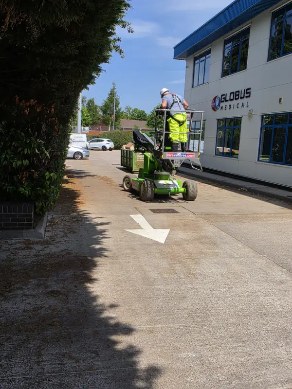 View from behind the MEWP with a white directional arrow on the tarmac and the operator on the basket reaching the building gutter line