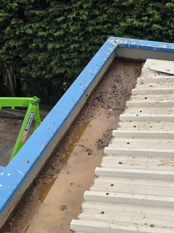 Oblique view of a gutter corner section with remaining mud at the base and the yellow-green MEWP basket in the foreground