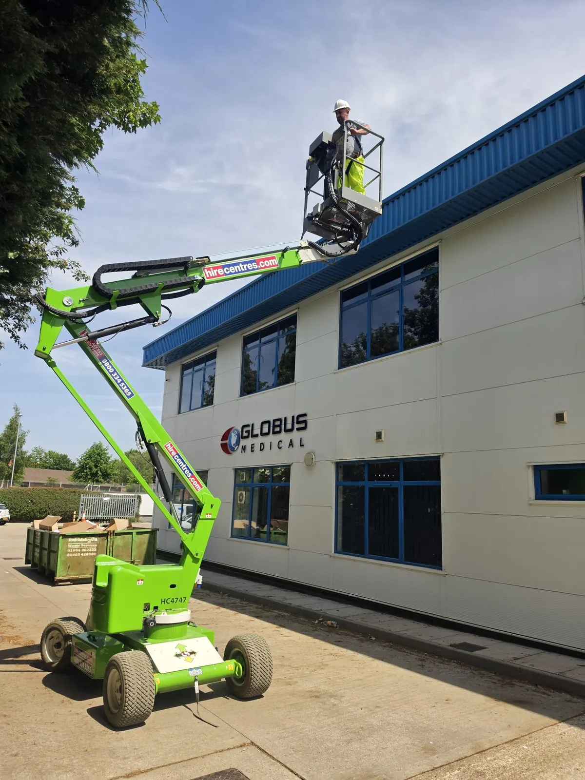 Operator on a Nifty articulated MEWP basket beside the Globus Medical UK building in Northampton, branded hire-centre boom in clear view