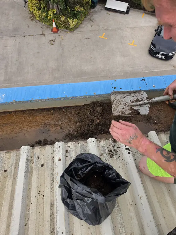 A scoop lifted vertically holding a compact block of wet mud out of the gutter line during clearing
