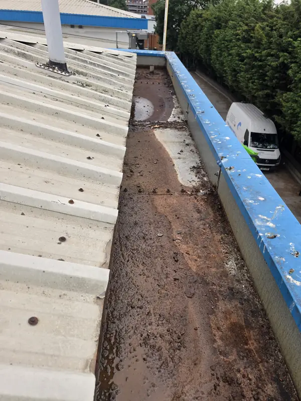 Long oblique view of an old gutter free of debris but with severe brown rust corrosion and visible perforations through the metal