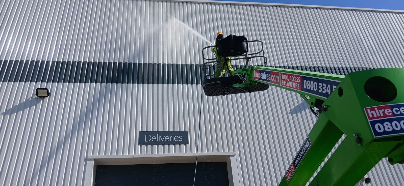MEWP cherry picker jet washing warehouse cladding at Partridges, Desborough