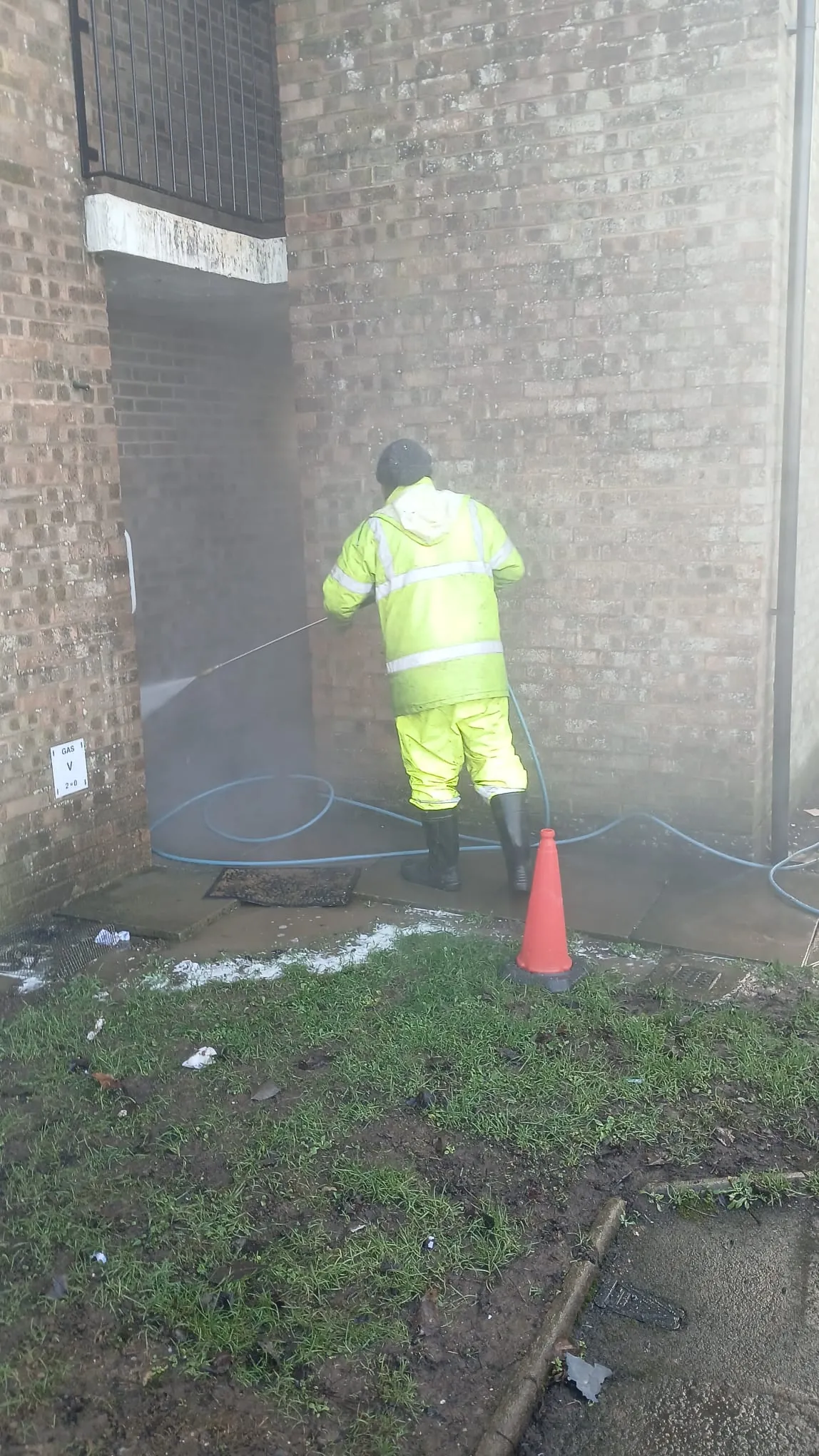 Worker in hi-vis PPE pressure washing brick undercroft passageway at residential apartment block, Northampton March 2026