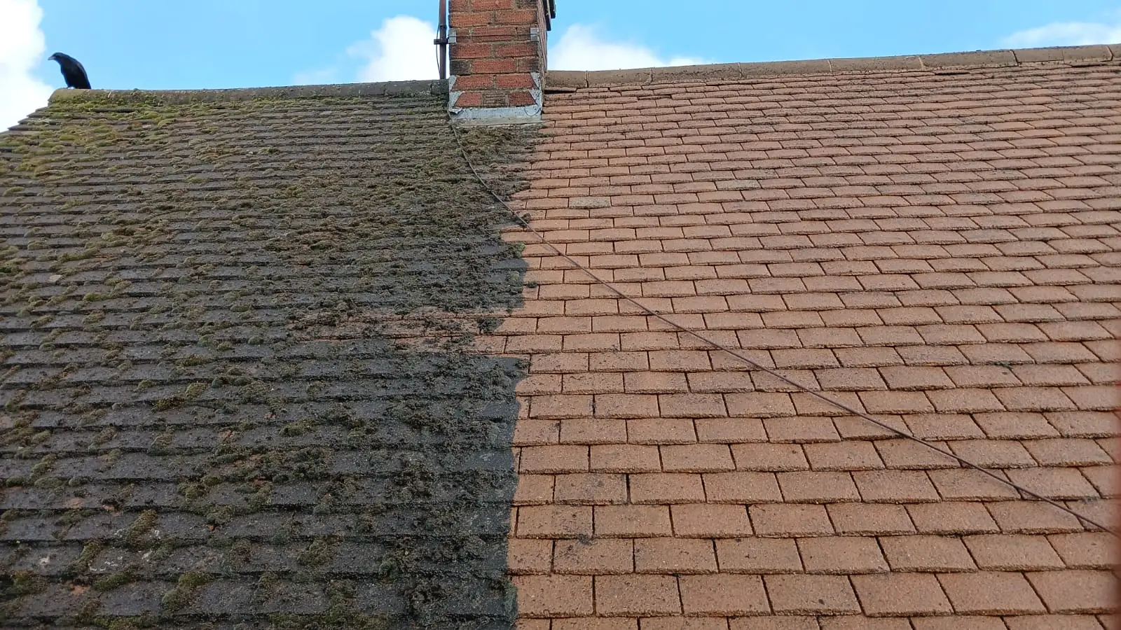 Roof with a central brick chimney half covered in green moss and half restored to clean terracotta tile