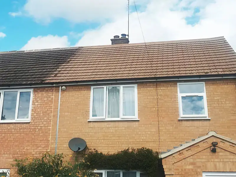 Semi-detached house roof part-cleaned with black algae staining on the left and clean brown tiles on the right