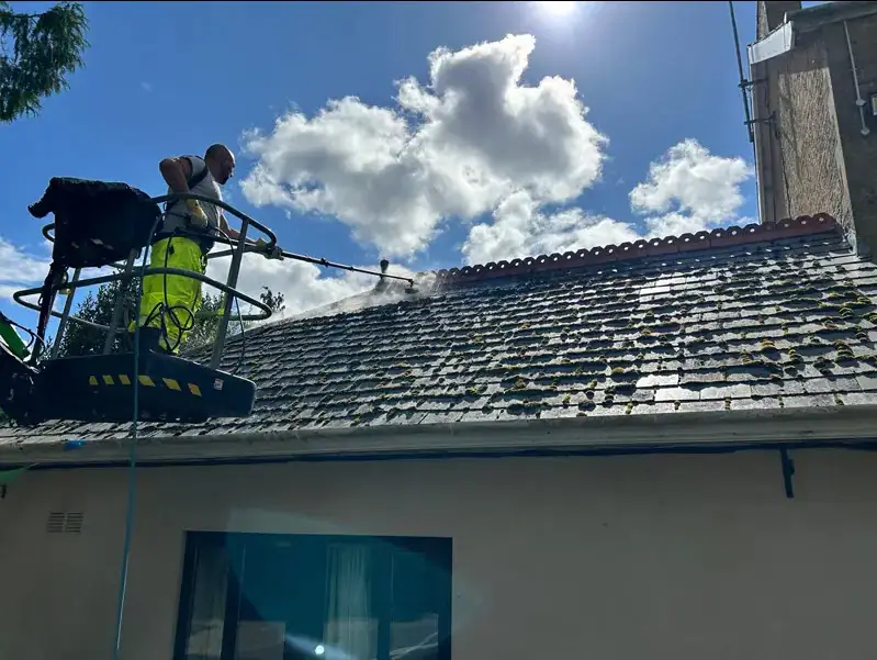 Hi-vis operative soft washing an old slate roof from a MEWP cherry picker with the low-pressure spray visible