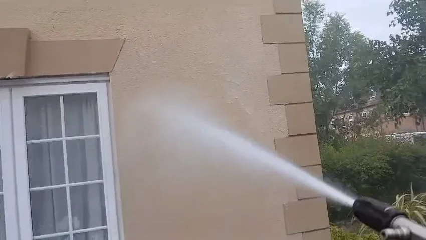 Professional cleaning operative applying softwash spray treatment to house render walls during algae removal cleaning process